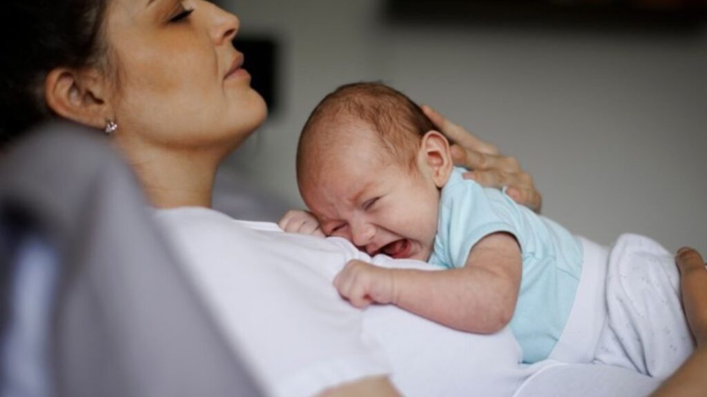 A baby crying in the arms of his mother as she's resting